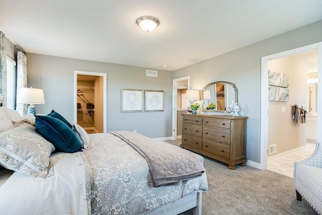 bedroom featuring light carpet, visible vents, a spacious closet, and baseboards