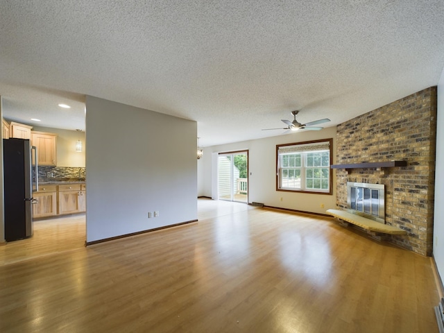 unfurnished living room with a textured ceiling, ceiling fan, light hardwood / wood-style floors, and a fireplace