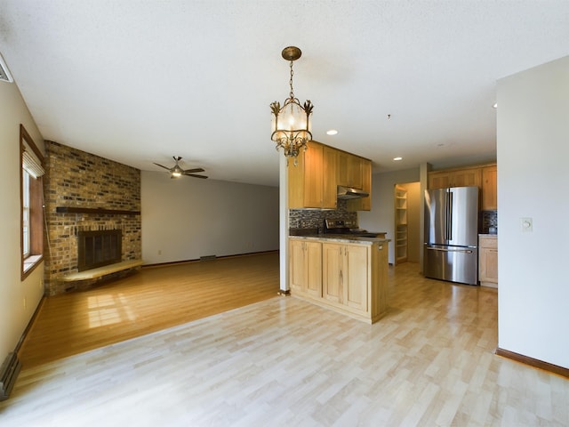 kitchen with appliances with stainless steel finishes, backsplash, light hardwood / wood-style floors, and a brick fireplace