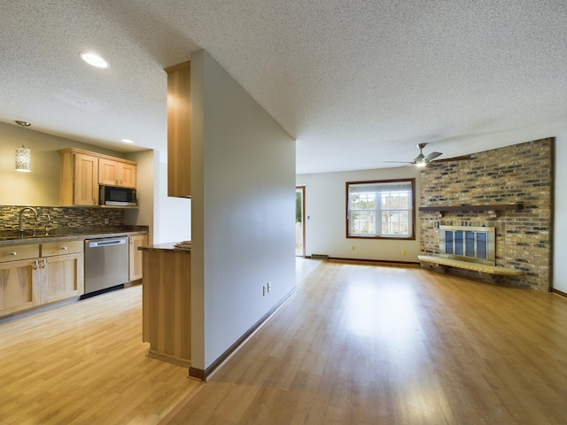 unfurnished living room with sink, light hardwood / wood-style flooring, ceiling fan, a textured ceiling, and a fireplace