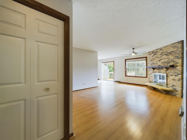 unfurnished living room with ceiling fan, a fireplace, a textured ceiling, and light hardwood / wood-style flooring