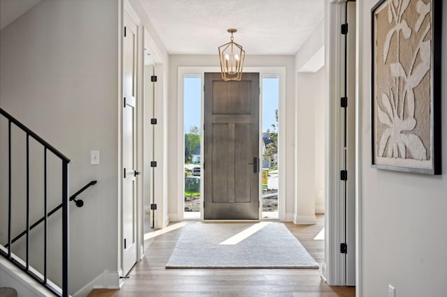 foyer entrance featuring a healthy amount of sunlight, light wood-type flooring, a textured ceiling, and a chandelier