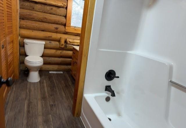 bathroom featuring toilet,  shower combination, hardwood / wood-style flooring, and rustic walls