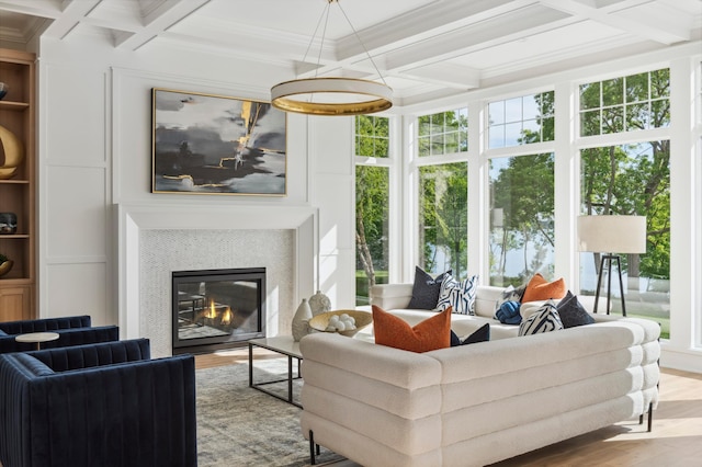 living room featuring a tile fireplace, coffered ceiling, built in features, crown molding, and hardwood / wood-style floors