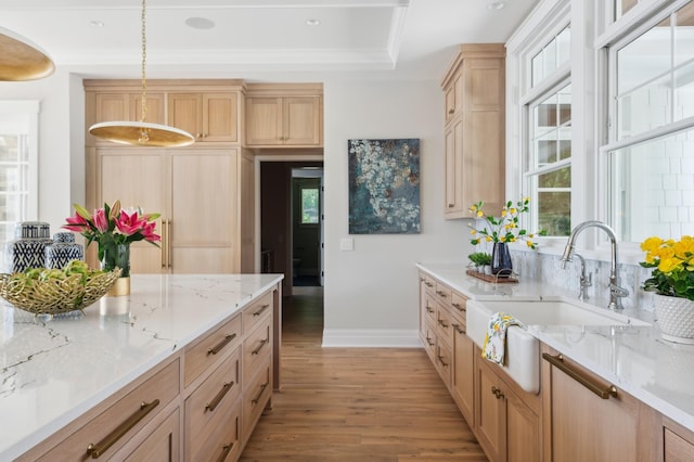 kitchen with sink, a raised ceiling, decorative light fixtures, light brown cabinetry, and light wood-type flooring