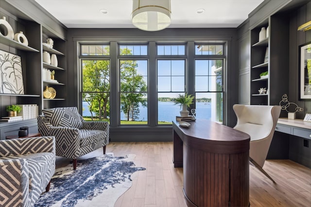 home office featuring built in shelves, a water view, built in desk, and light hardwood / wood-style flooring