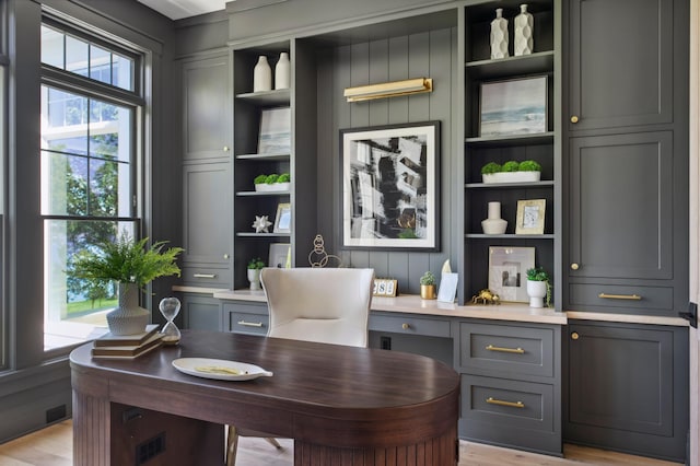 office featuring light wood-type flooring, built in desk, and a wealth of natural light