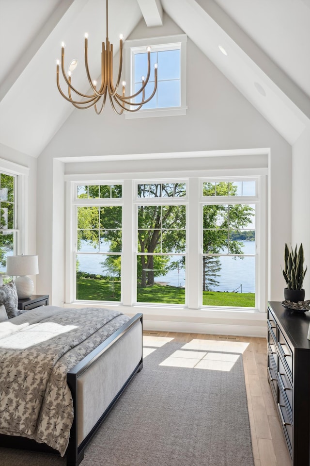 bedroom featuring lofted ceiling with beams, light hardwood / wood-style floors, a water view, and an inviting chandelier