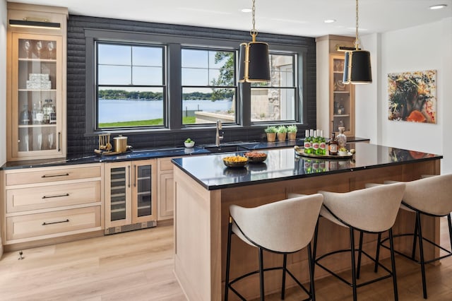 bar featuring beverage cooler, sink, a water view, light hardwood / wood-style flooring, and hanging light fixtures