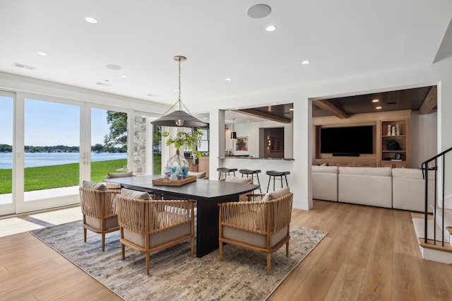 dining room featuring beam ceiling, light hardwood / wood-style flooring, and a water view