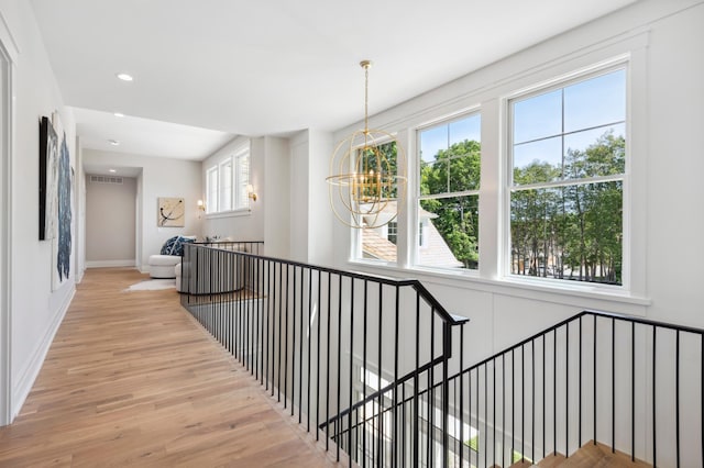 hall featuring a chandelier, light wood-type flooring, and plenty of natural light