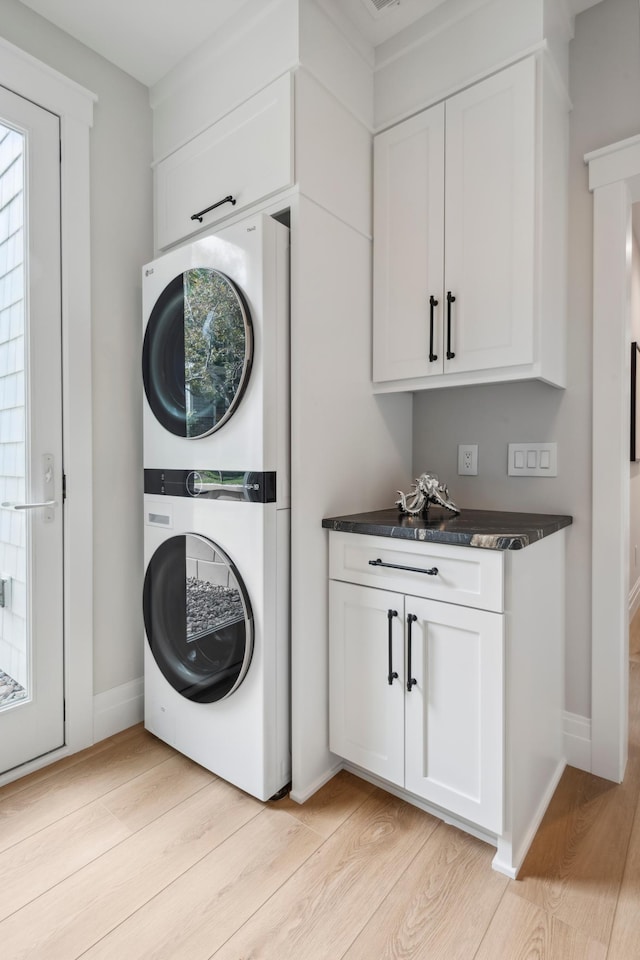 washroom featuring light hardwood / wood-style floors, cabinets, and stacked washing maching and dryer