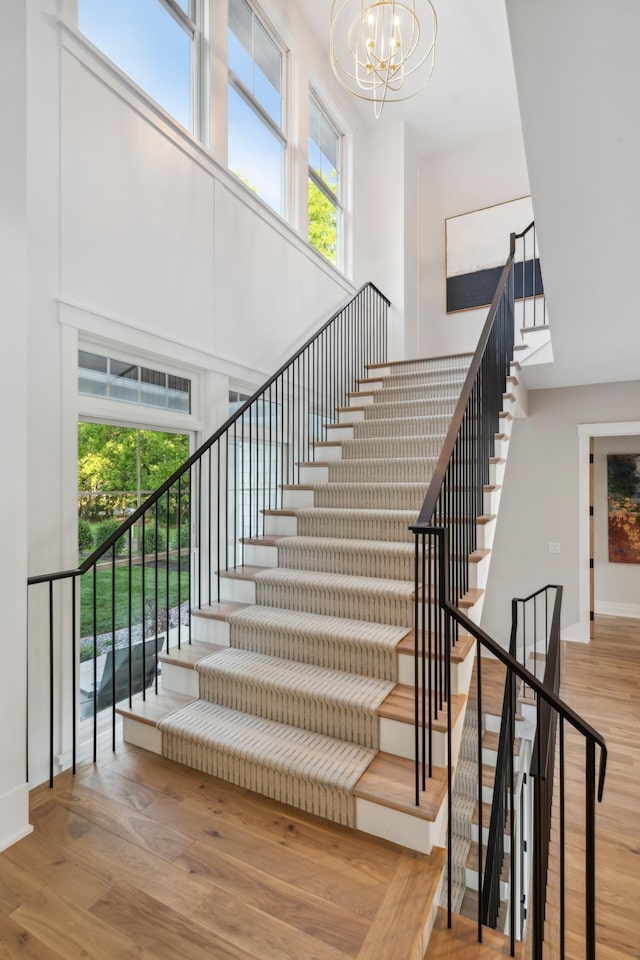 stairway featuring a notable chandelier, wood-type flooring, and a towering ceiling