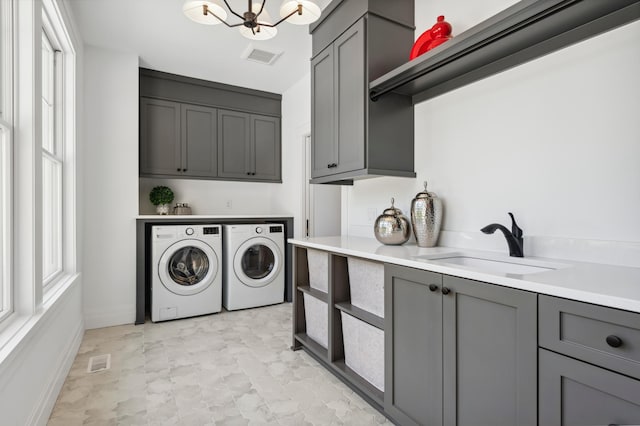 clothes washing area with cabinets, washer and clothes dryer, sink, an inviting chandelier, and plenty of natural light