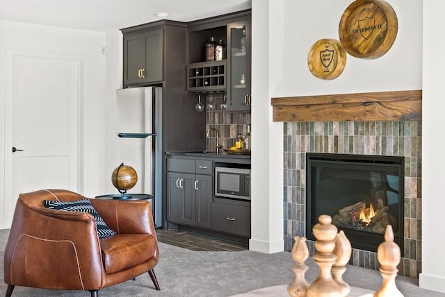 bar featuring decorative backsplash, a tiled fireplace, appliances with stainless steel finishes, wet bar, and a sink