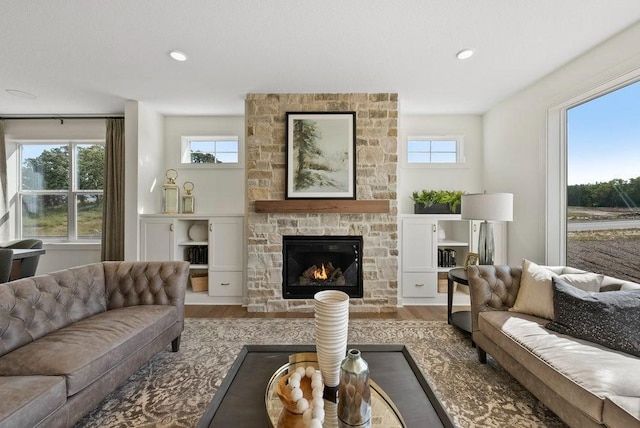 living room featuring recessed lighting, wood finished floors, and a stone fireplace