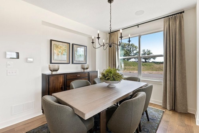 dining area with light wood finished floors, baseboards, visible vents, and an inviting chandelier