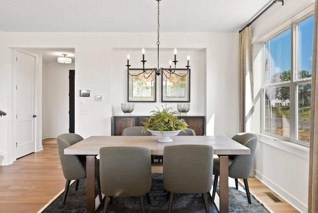 dining space featuring an inviting chandelier, baseboards, visible vents, and wood finished floors