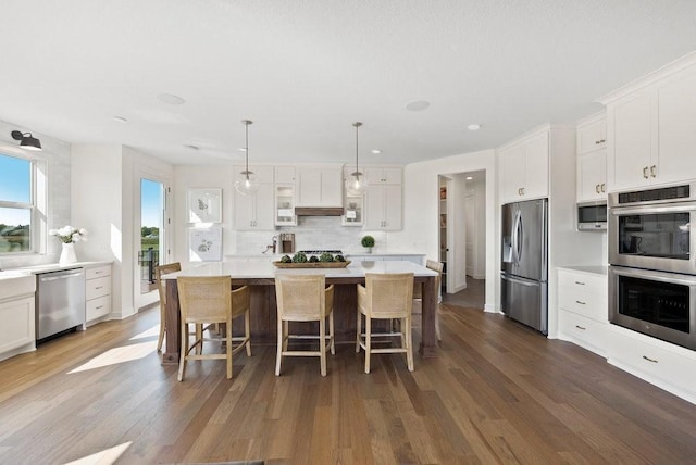 kitchen with light countertops, appliances with stainless steel finishes, a kitchen island, and decorative light fixtures