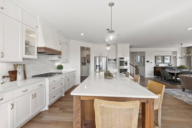 kitchen with custom range hood, a kitchen island, stainless steel appliances, a kitchen bar, and pendant lighting