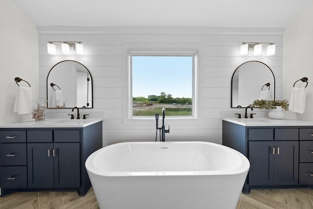 full bath featuring a soaking tub, two vanities, and a sink