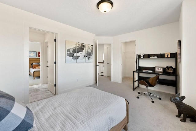 bedroom with light carpet, baseboards, a walk in closet, a textured ceiling, and a closet