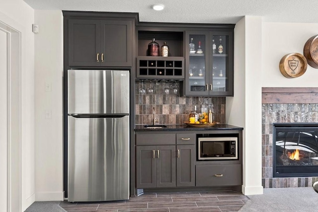 bar with indoor wet bar, decorative backsplash, appliances with stainless steel finishes, a sink, and a tile fireplace