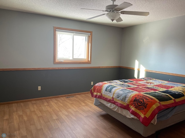 bedroom with a textured ceiling, light wood-type flooring, and ceiling fan