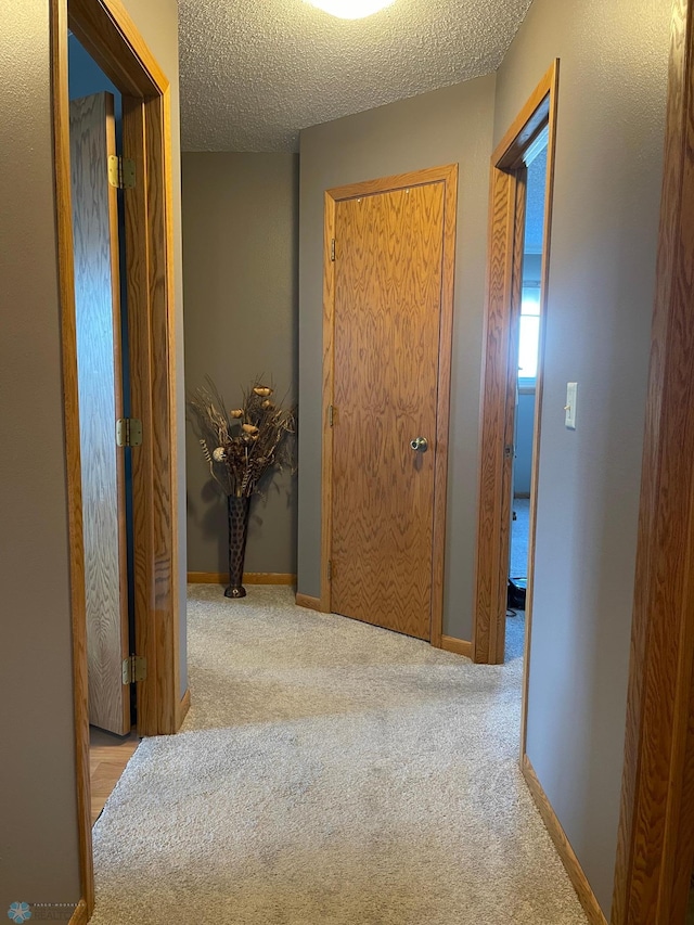 corridor with a textured ceiling and light colored carpet