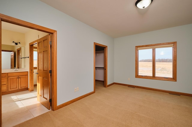 unfurnished bedroom featuring ensuite bath, sink, light colored carpet, a walk in closet, and a closet