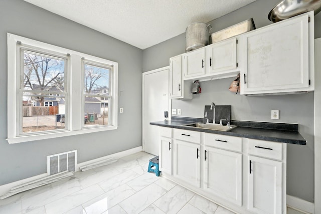 kitchen featuring baseboards, visible vents, dark countertops, marble finish floor, and a sink