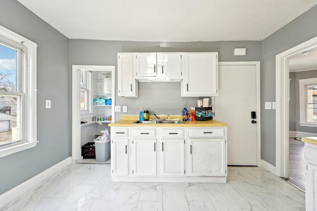 kitchen with marble finish floor, light countertops, white cabinetry, a sink, and baseboards