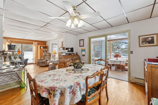 dining room featuring ceiling fan, a drop ceiling, a baseboard heating unit, and light hardwood / wood-style floors