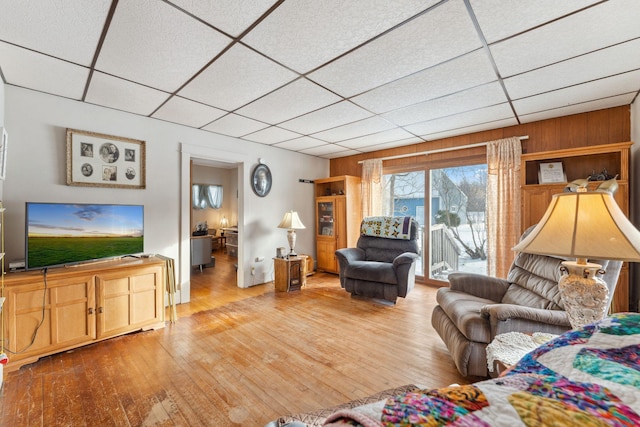 living room featuring a paneled ceiling, light hardwood / wood-style flooring, and wooden walls