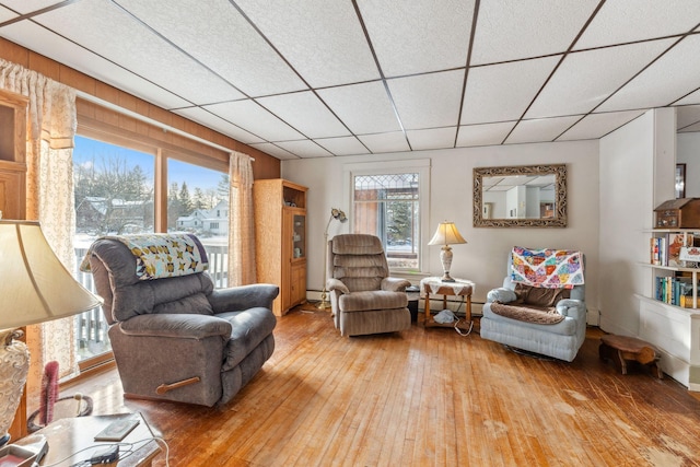 living room featuring baseboard heating, plenty of natural light, a drop ceiling, and hardwood / wood-style floors