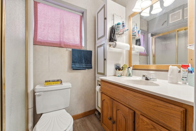 bathroom featuring toilet, hardwood / wood-style flooring, tile walls, walk in shower, and vanity