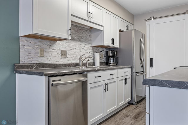 kitchen with white cabinets, stainless steel appliances, tasteful backsplash, sink, and a barn door