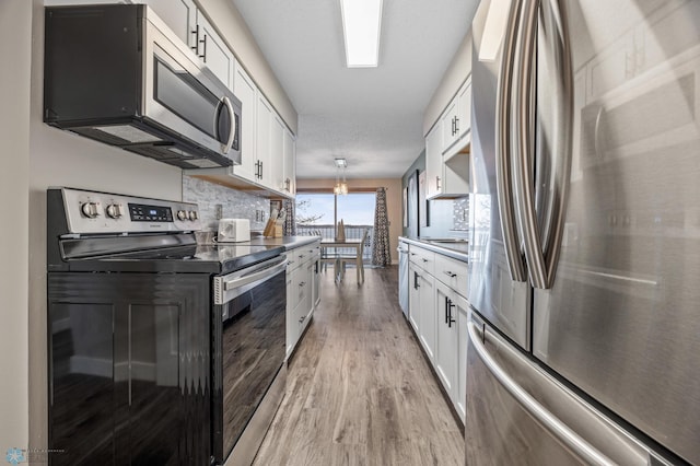 kitchen featuring pendant lighting, white cabinets, stainless steel appliances, and light wood-type flooring