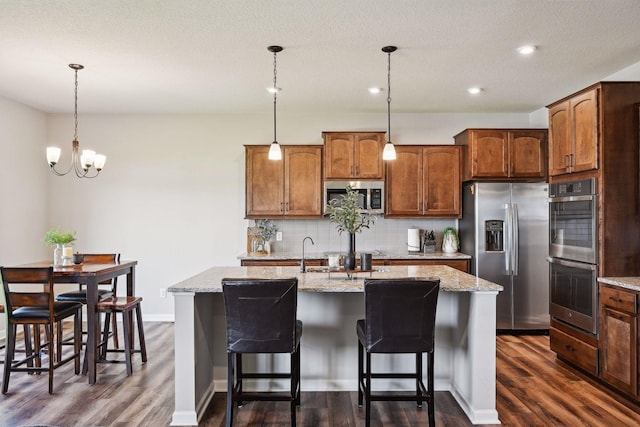 kitchen with dark wood-type flooring, a kitchen bar, appliances with stainless steel finishes, a kitchen island with sink, and backsplash