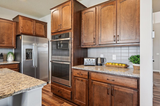 kitchen featuring stainless steel appliances, light stone countertops, dark wood-style flooring, and backsplash