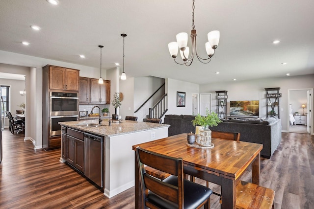 kitchen featuring an island with sink, appliances with stainless steel finishes, dark wood-style flooring, a sink, and decorative light fixtures