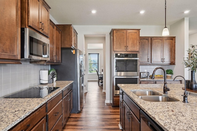 kitchen featuring hanging light fixtures, a sink, dark wood finished floors, stainless steel appliances, and light stone counters