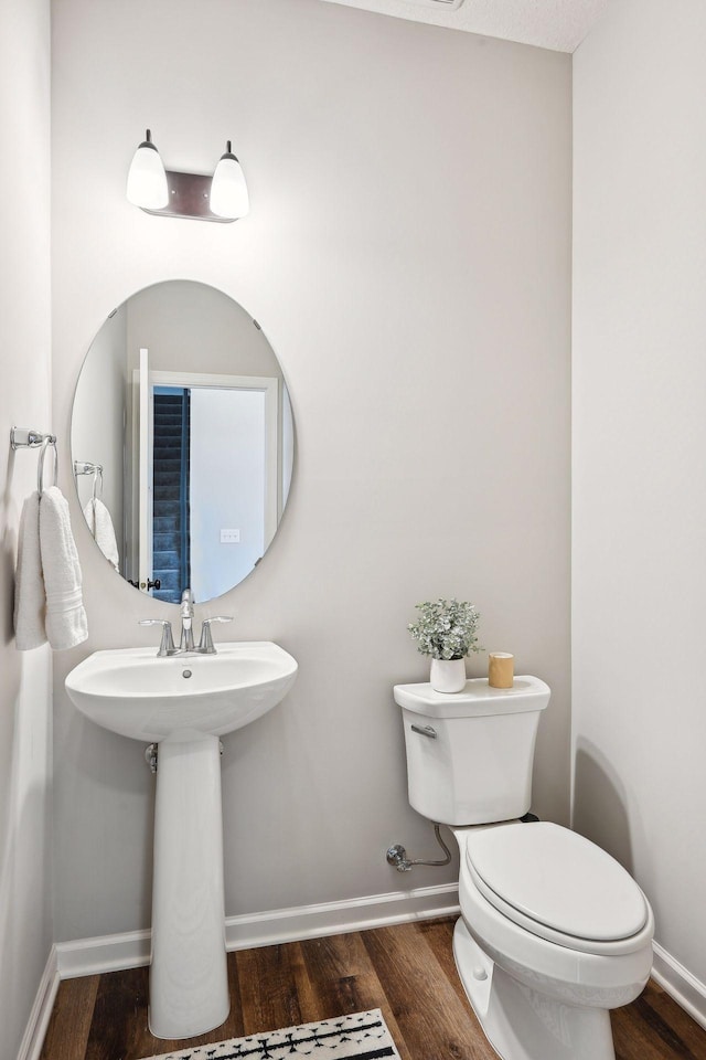 half bath with baseboards, toilet, and wood finished floors