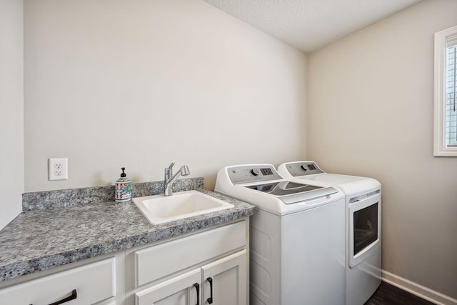 washroom featuring baseboards, a textured ceiling, cabinet space, washer and dryer, and a sink