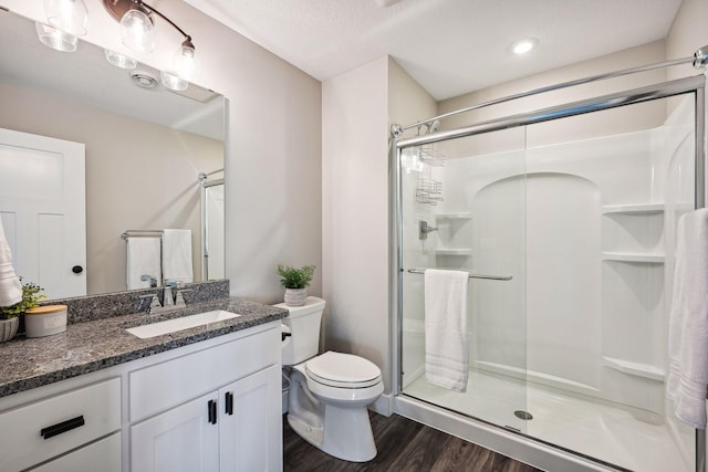 bathroom featuring toilet, vanity, a stall shower, and wood finished floors
