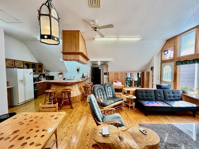 living room with ceiling fan, light wood-type flooring, a textured ceiling, and lofted ceiling