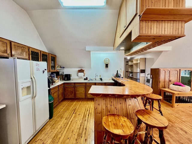 kitchen featuring sink, vaulted ceiling, light wood-type flooring, white fridge with ice dispenser, and kitchen peninsula