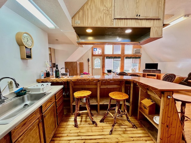 bar featuring a textured ceiling, light hardwood / wood-style flooring, sink, and vaulted ceiling