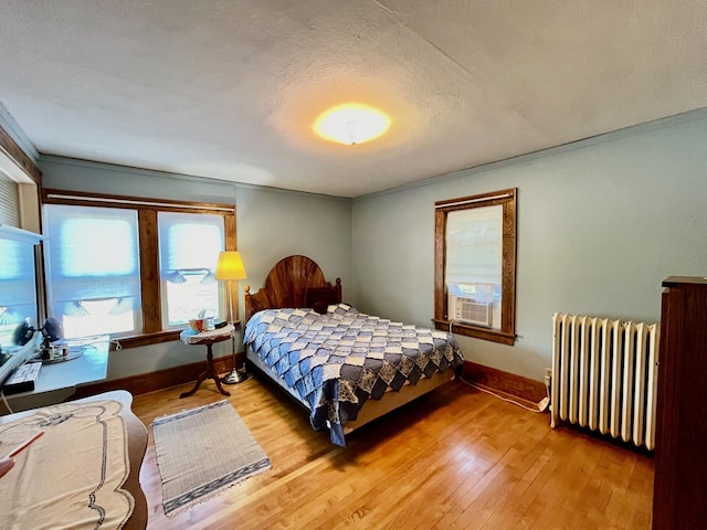 bedroom with radiator heating unit, cooling unit, wood-type flooring, and a textured ceiling