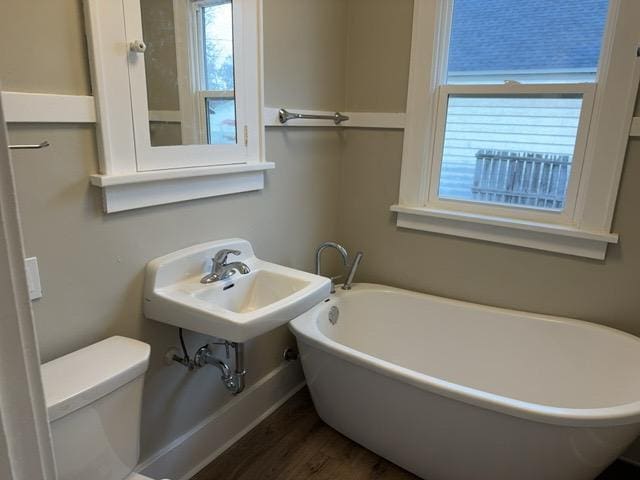 bathroom with a bath, toilet, and wood-type flooring